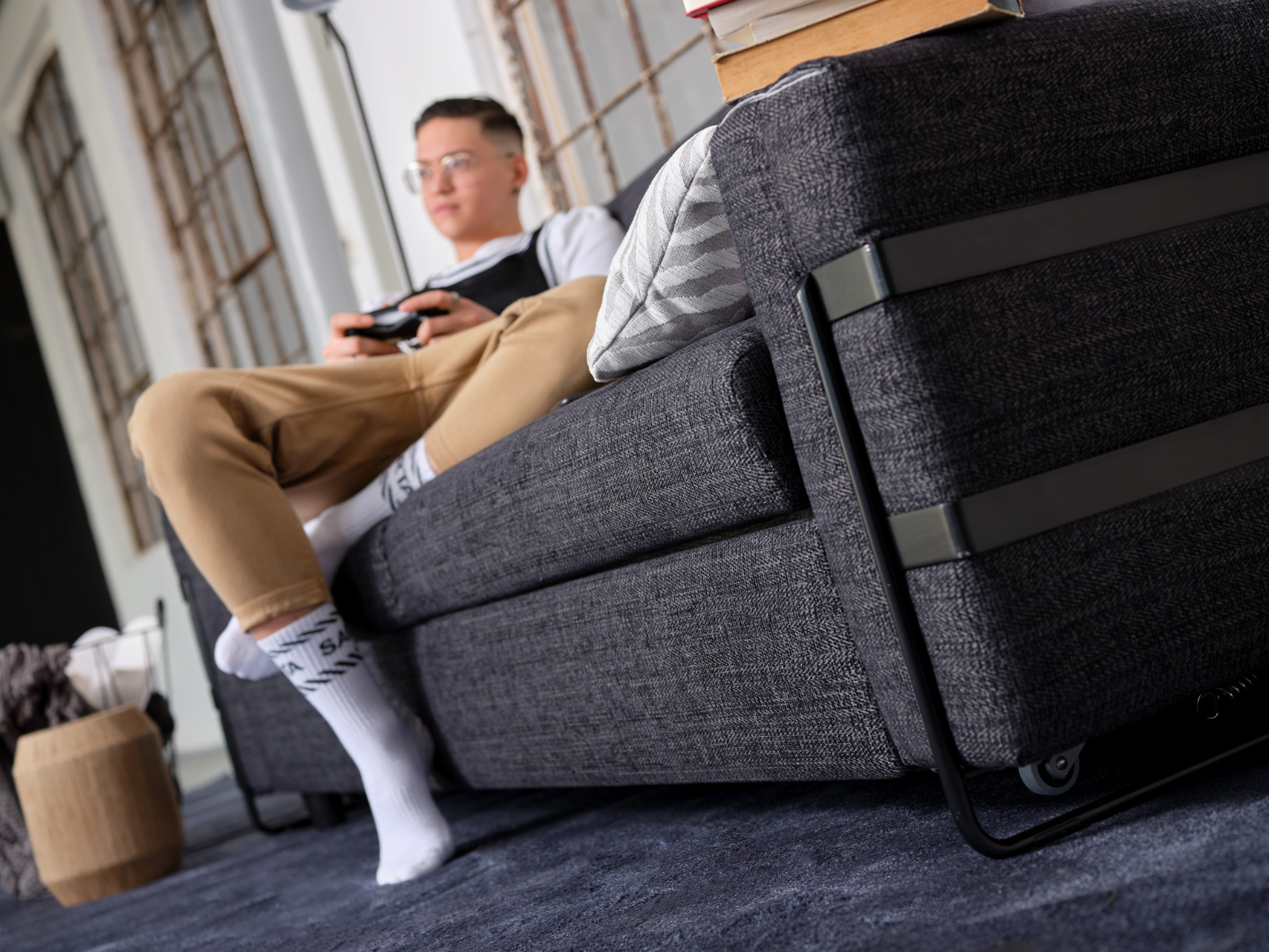 DORADO_7 Spielender junger Mann auf einem grauen Schlafsofa