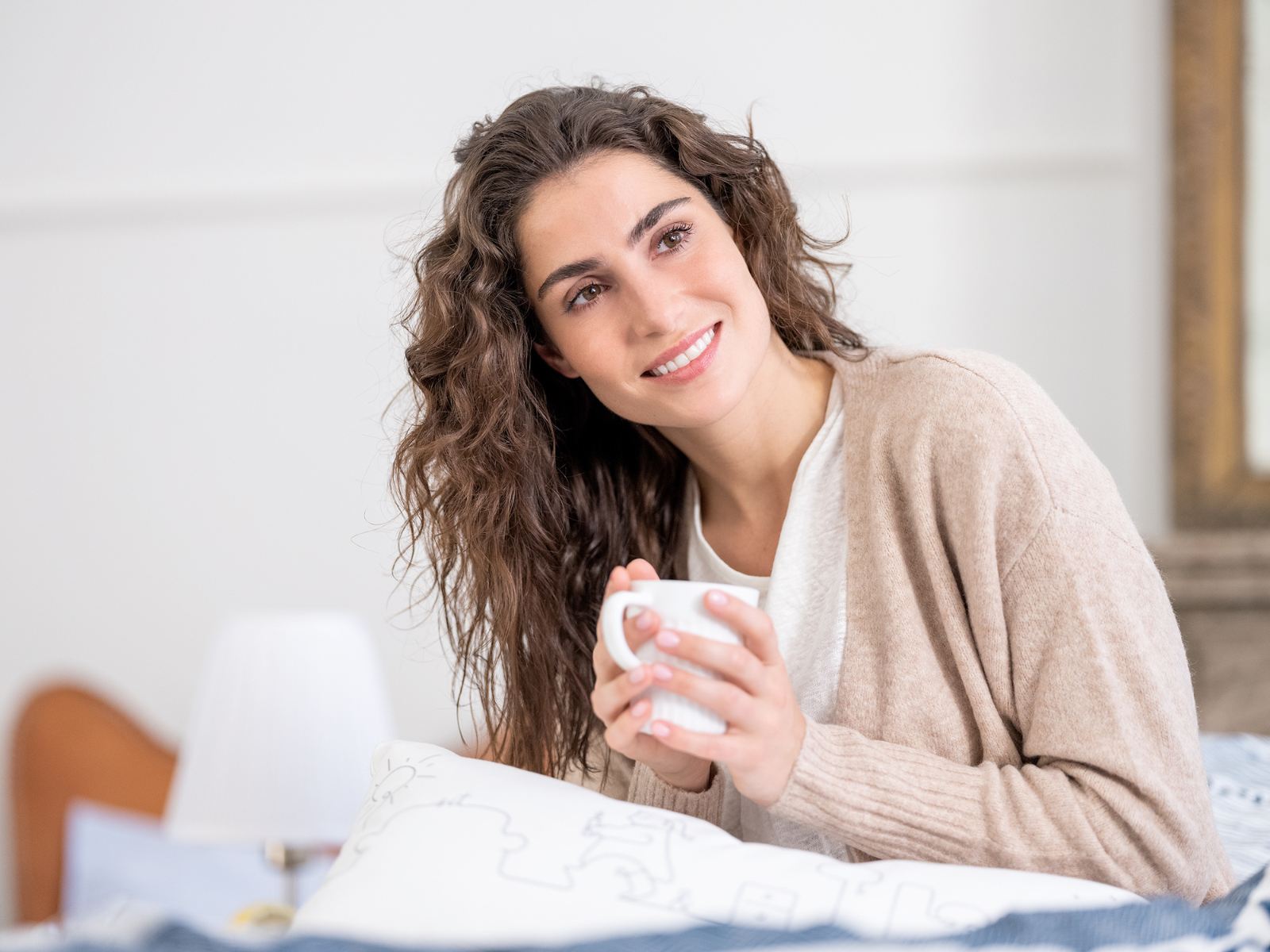 SESIDO_IMPRESSIONS_3 Frau guckt in die Ferne während sie ihren Tee hält auf einem geöffneten Schlafsofa